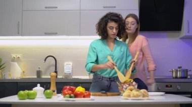 Kadın arkadaşlar cam kasede salata karıştırıyor tuz, mutfak ve kaliteli zaman ekliyorlar.