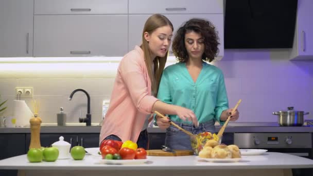 Pareja de lesbianas degustando ensalada fresca de bowl, besándose en la mejilla, cuidado familiar — Vídeo de stock