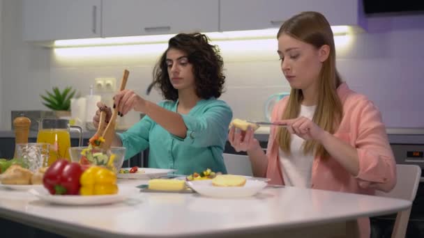 Dos mujeres jóvenes almorzando en casa, poniendo ensalada en el plato, amistad — Vídeo de stock