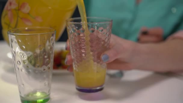 Kvinna häller apelsinjuice i glas på bordet, kvinnliga vänner dricker juice — Stockvideo