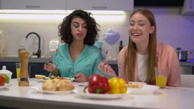 Bayan oda arkadaşları konuşuyor, evde taze salata yiyor, birlikte akşam yemeği yiyorlar.