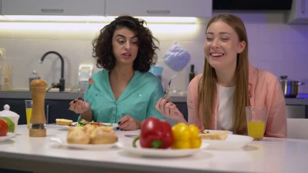 Compañeras de cuarto hablando, comiendo ensalada fresca en casa, cenando juntas — Vídeo de stock