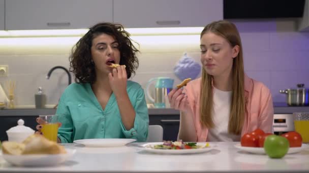 Gelukkige zussen eten pizza thuis, drinken sinaasappelsap, familie cheat maaltijd — Stockvideo