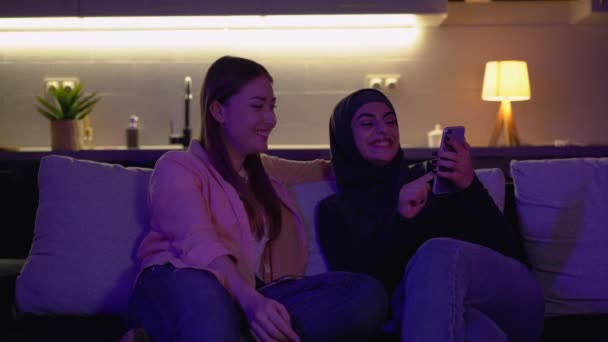 Multiculturele vrouwelijke vrienden kijken naar smartphone, glimlachen plezier thuis — Stockvideo
