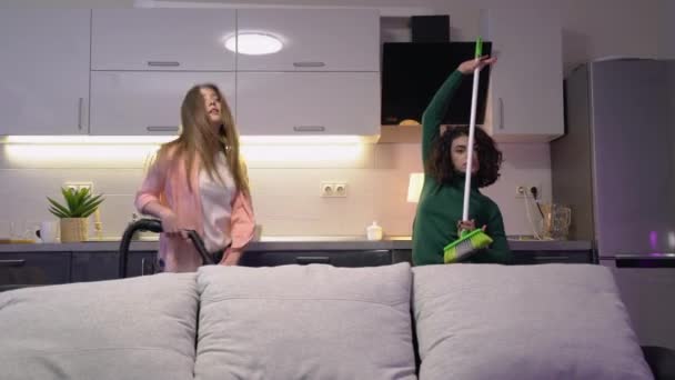 Активні молоді жінки танцюють з пилососом і мітлою, прибирають квартиру — стокове відео