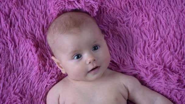Adorable bebé con cara curiosa acostado en una manta suave, ambiente de confort en el hogar — Vídeo de stock