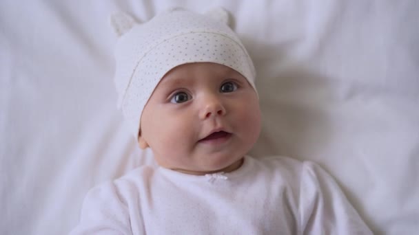 Cara infantil curiosa, bebé con ropa de algodón acostado en la cama, amor y cuidado familiar — Vídeo de stock