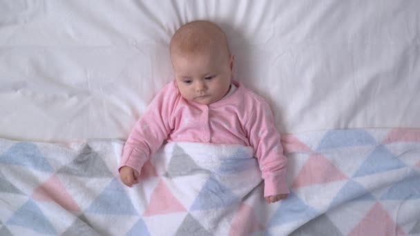 かわいい赤ちゃんはカラフルな毛布で覆われたベッドの上に横たわって、周りを見回す — ストック動画