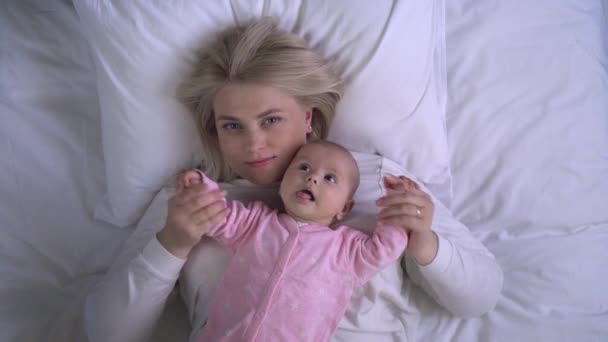 Anyaság szeretet és gondozás, fiatal anya játszik baba kezét, belenéz a kamerába — Stock videók