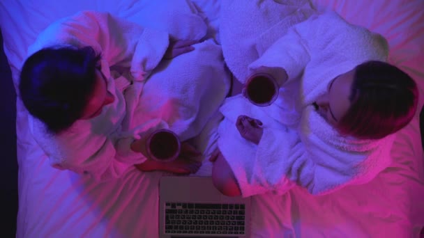 Két lány csörömpöl borospoharak az ágyon, élvezi a szép romantikus beszélgetés — Stock videók