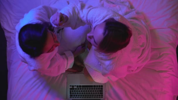 Amici donne che spennano sopracciglia con pinzette, seduti sul letto in accappatoi — Video Stock