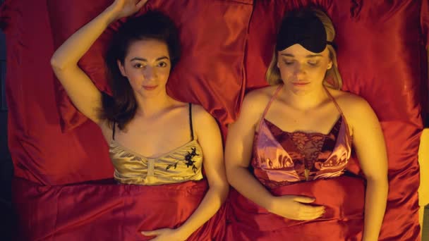 Flörtölő lányok fekszenek selyem ágyneműn, csábítóan néznek a kamerába, kísértés