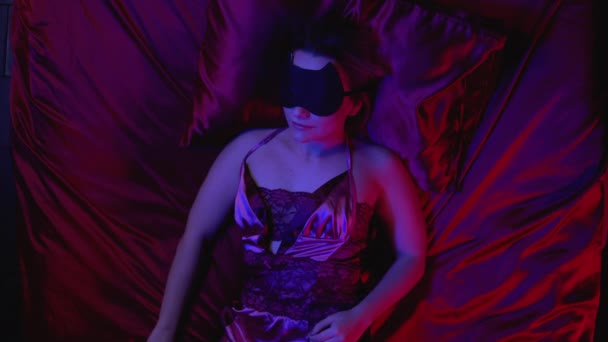 Beautiful young woman sleeping on silk bed linen alone, sleep mask on face — Stock Video