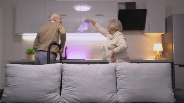 Fröhliches altes Paar, das zusammen mit Staubsauger und Lappen tanzt, Glück — Stockvideo