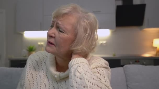 Oude vrouw voelt zich ongemakkelijk in de nek, zit thuis, ruggenmergziekte, gezondheidszorg — Stockvideo