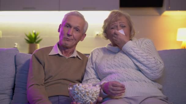 Пожилые муж и жена смотрят мелодраму дома, плачущая женщина вытирает слезы — стоковое видео