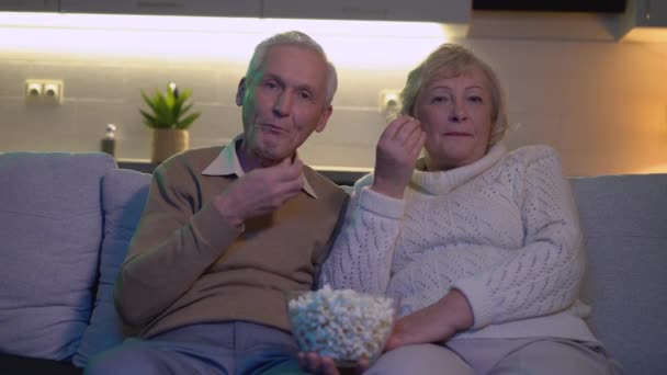 Старший муж и жена смотрят телевизор дома, едят попкорн, отдыхают — стоковое видео