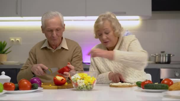 Старик и женщина режут свежие овощи на кухне, наслаждаясь кулинарным хобби — стоковое видео