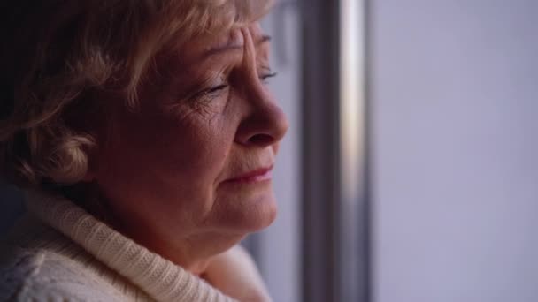 Szomorú idős nő sír közel ablak egyedül, szegénység idős korban, pénzügyi válság — Stock videók