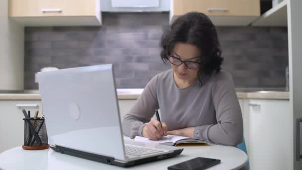 Schöne Frau schreibt in Notizbuch, arbeitet am Laptop, Online-Bildung — Stockvideo