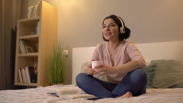 Mulher atraente em fones de ouvido cantando, ouvindo música, relaxando em casa — Vídeo de Stock