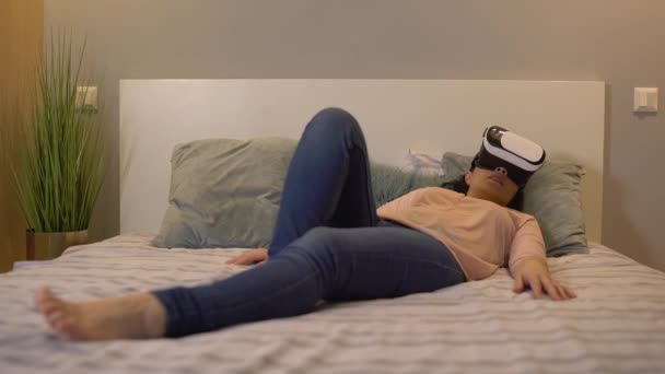 Excited young woman watching adult video in vr headset, relaxing on bed alone — 비디오