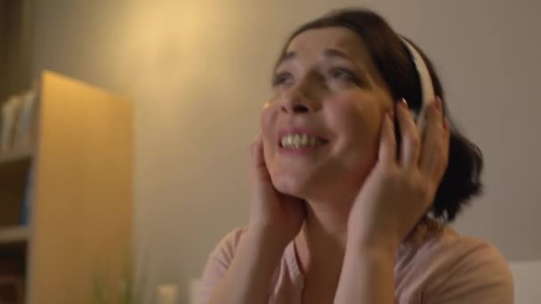 快乐的中年妇女在耳机里听着最喜欢的音乐，在家里放松 — 图库视频影像