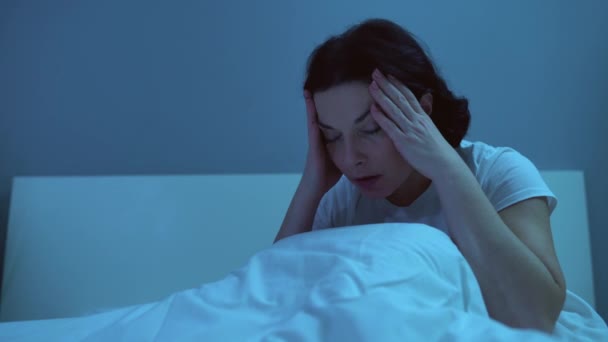 Álmatlan nő dörzsöli a fejét az ágyban, éjjel migréntől szenved, egészségügyi probléma — Stock videók