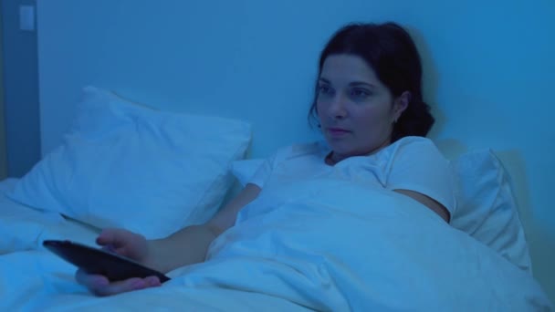 Jeune femme commutation de chaînes de télévision avec télécommande, couché dans le lit seul — Video