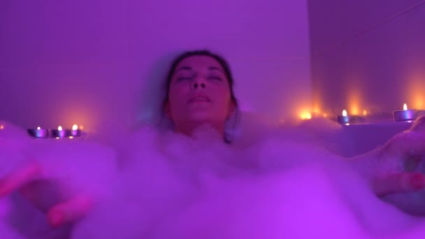 Femme détendue couchée dans un bain mousseux, jouissant d'une atmosphère tranquille de lumière de bougie — Video