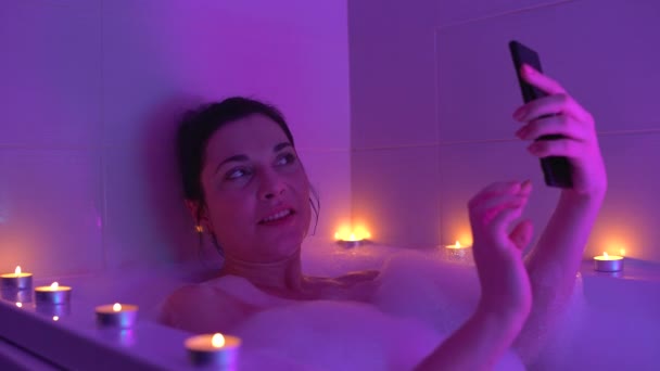 Romantik banyo atmosferinde akıllı telefondan selfie çeken mutlu kadın, rahatla. — Stok video