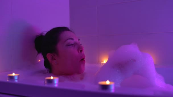 Heureuse jeune femme jouant avec la mousse dans le bain de lumière de bougie, romantique se détendre à la maison — Video