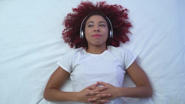 Jovencita alegre en auriculares relajándose en la cama, disfrutando de música favorita, descanso — Vídeo de stock