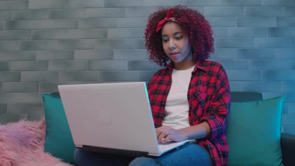 Женщина-студентка из Африки печатает на ноутбуке, сидит на диване, делает домашнюю работу, приложение — стоковое видео