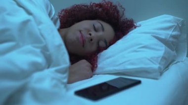 Akıllı telefonuyla yatakta uyuyan genç bir kız, geceleri mesajları kontrol ediyor.