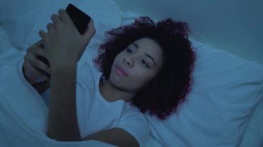 Akıllı telefon uygulaması üzerinden mesaj gönderen genç bir kız, yatakta uzanıp sohbet ediyor.