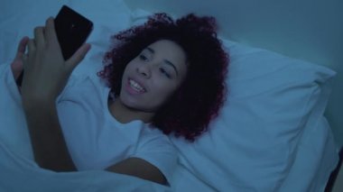 Mutlu üniversite öğrencisi akıllı telefondan fotoğraf çekiyor, geceleri yatakta yatıyor.