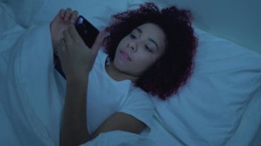 Çekici Afrikalı kadın geceleri telefonda fotoğraf kaydırıyor, flört başvurusu yapıyor.