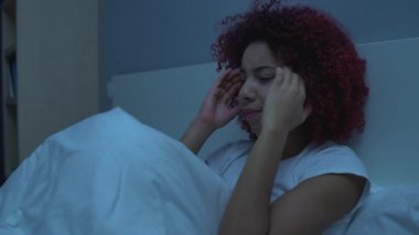 Genç bir kadın baş ağrısı çekiyor, geceleri yatakta oturuyor, şakaklara masaj yapıyor, sağlığını koruyor.
