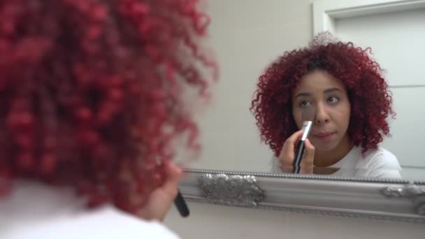 Afro-american woman applying makeup with a brush in front of mirror, cosmetics — Stock Video