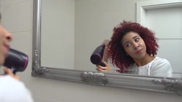 Young woman drying curly hair in bathroom, smiling in mirror, hairstyle tips — 비디오