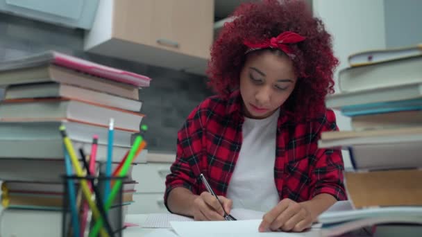 Chica adolescente sobrecargada de trabajo escribiendo en cuaderno, pilas de libros en la mesa, agotamiento escolar — Vídeo de stock