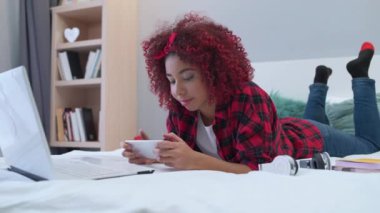 Modern bayan ergen akıllı telefondan internet sayfalarını izliyor, evde yatakta yatıyor.