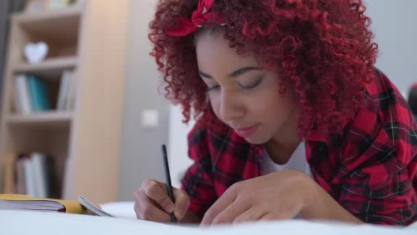 Έφηβος μαθητής γράφει στο σημειωματάριο, ξαπλωμένος στο κρεβάτι, εργάζεται σε σχολική εργασία — Αρχείο Βίντεο