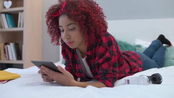 Młoda kobieta czytająca książkę elektroniczną na łóżku, ciesząca się hobby nowoczesnym gadżetem — Wideo stockowe
