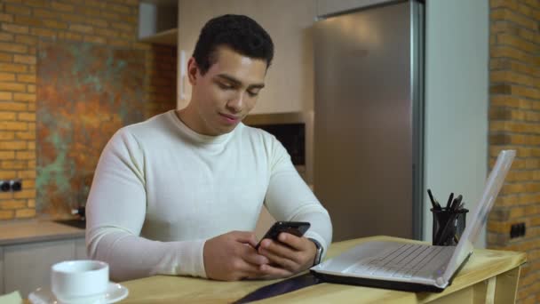 Joven freelancer masculino escribiendo en el teléfono inteligente, utilizando la aplicación de la bolsa — Vídeos de Stock
