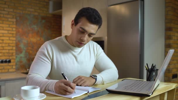 Homem de negócios árabe escrevendo no caderno, sentado na frente do laptop, profissão — Vídeo de Stock