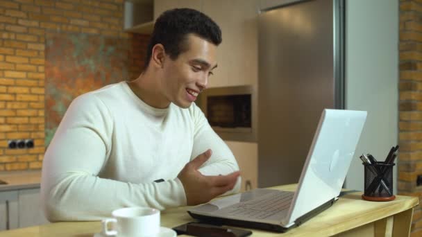 Счастливый смешанный мужчина разговаривает с другом онлайн, используя приложение для ноутбука, репетитор — стоковое видео