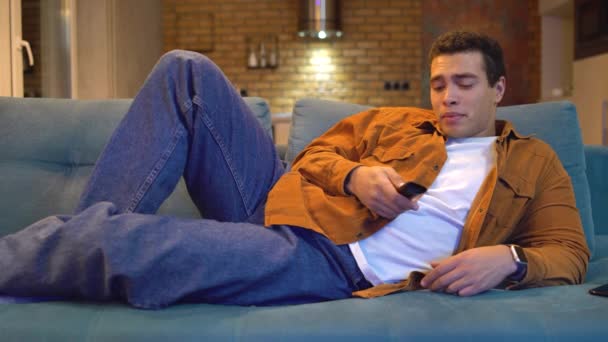 Bored man switching tv channels on couch home, laughing at comedy show, rest — Stock Video