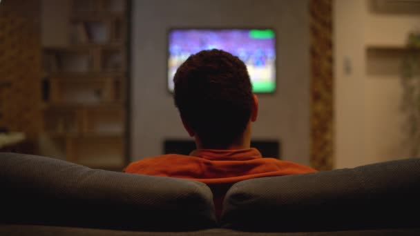 Скучный спортивный болельщик смотрит плохую игру по телевизору, разочарован счетом, вид сзади — стоковое видео